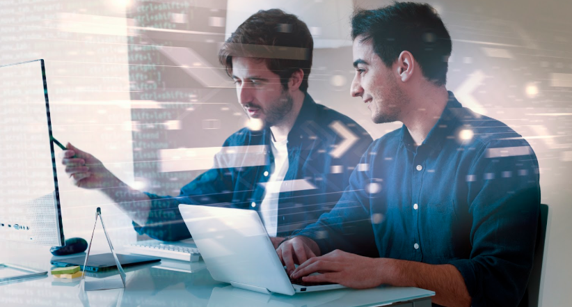 A software engineer and a developer working collaboratively on a project, with laptops and code visible in the background.